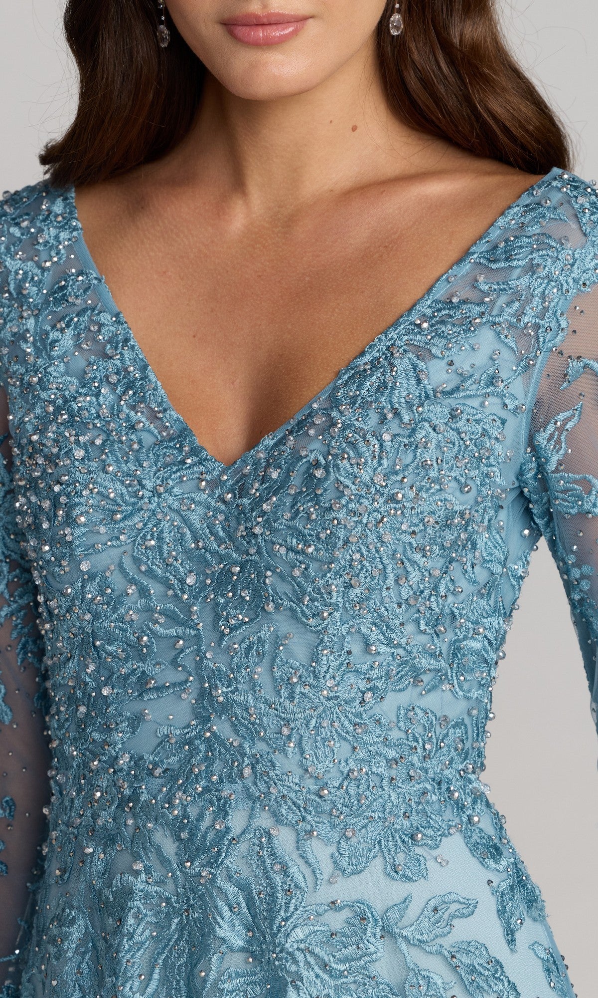A woman wearing the Mac Duggal 20409 Long Sleeve Lace Formal Gown, a light blue dress with intricate beading and embroidery and a deep V-neckline—an elegant choice for mother of the bride.